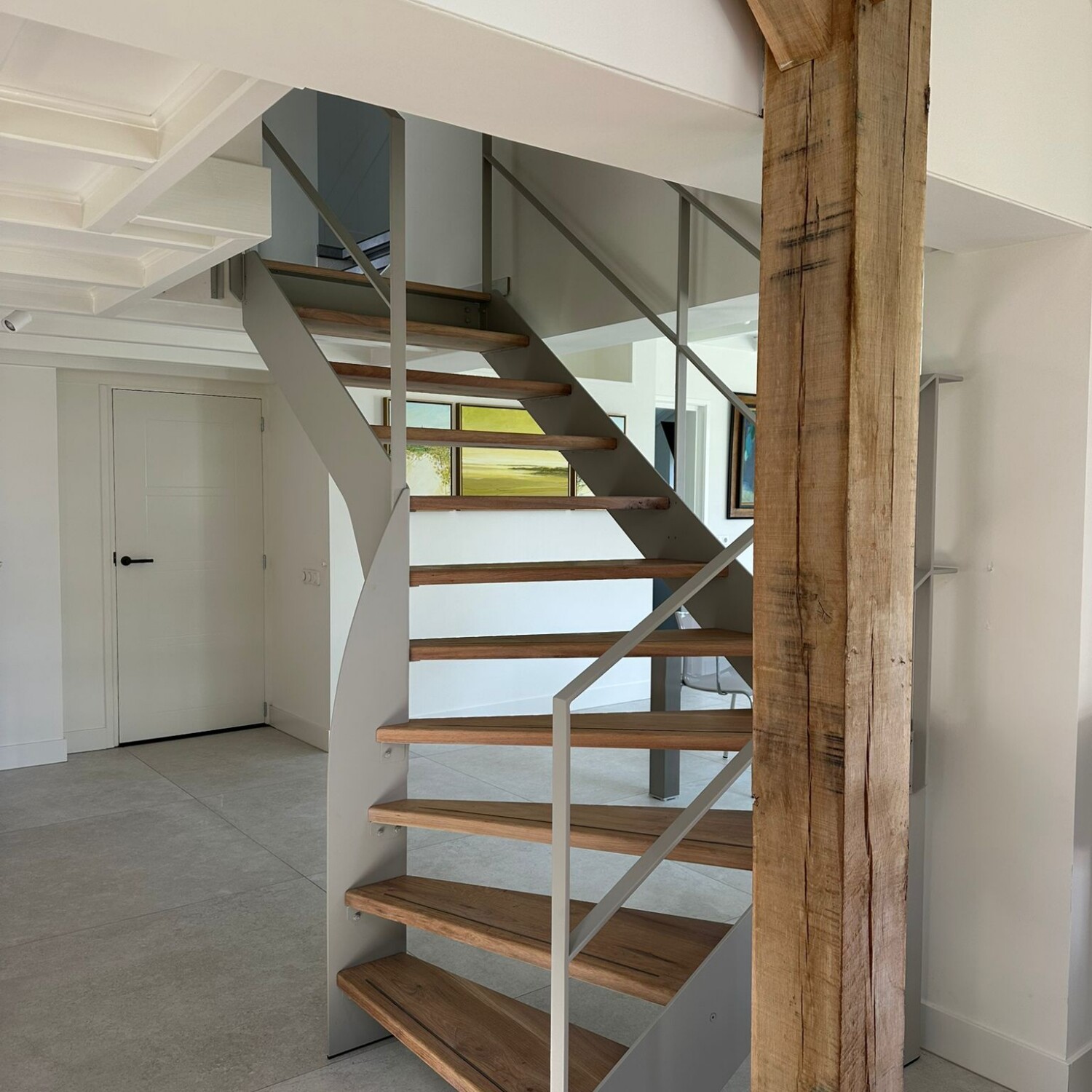 Moderne open stalen trap met een lichtgrijze coating, massief eikenhouten treden en een minimalistische stalen balustrade.